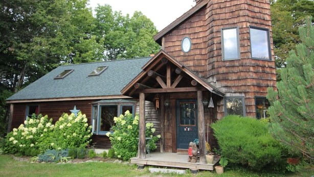 Una casa di legno rustica con una torre imponente, un portico con una statua di orso e un giardino curato.