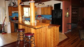 Una cucina con mobili in legno, un'isola centrale con sgabelli, illuminazione a sospensione e un frigorifero nero.