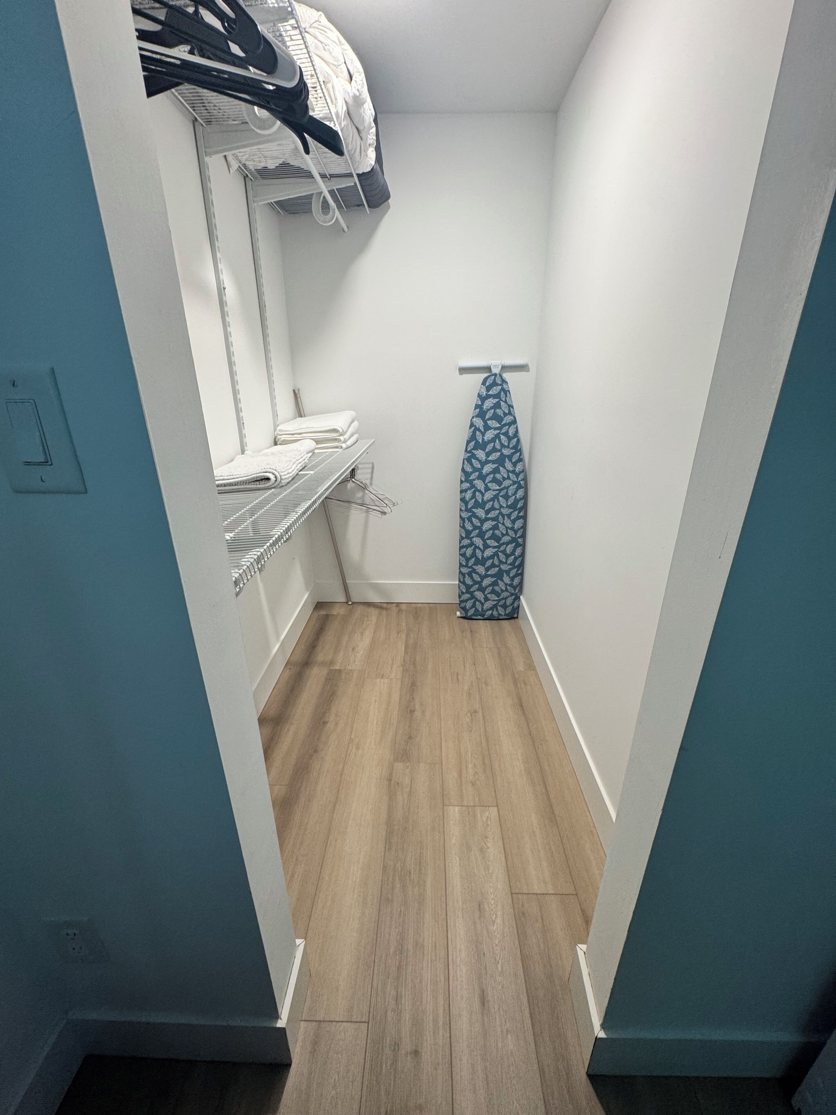 A narrow hallway with a wooden floor, a clothes rack with folded clothes, and a hanging garment on a wall-mounted rack.