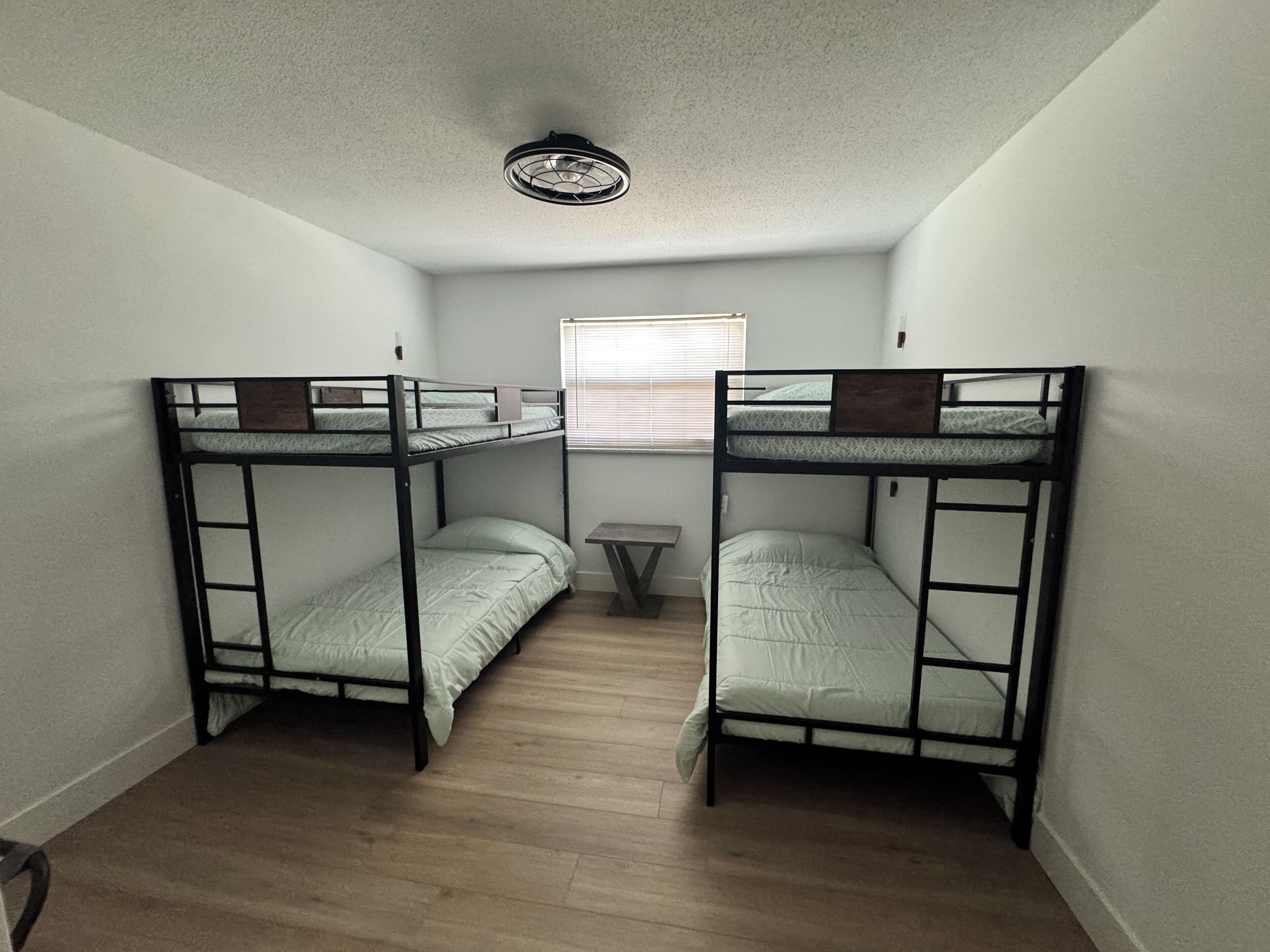 A small, compact room with two bunk beds, a small table, and a ceiling fan.