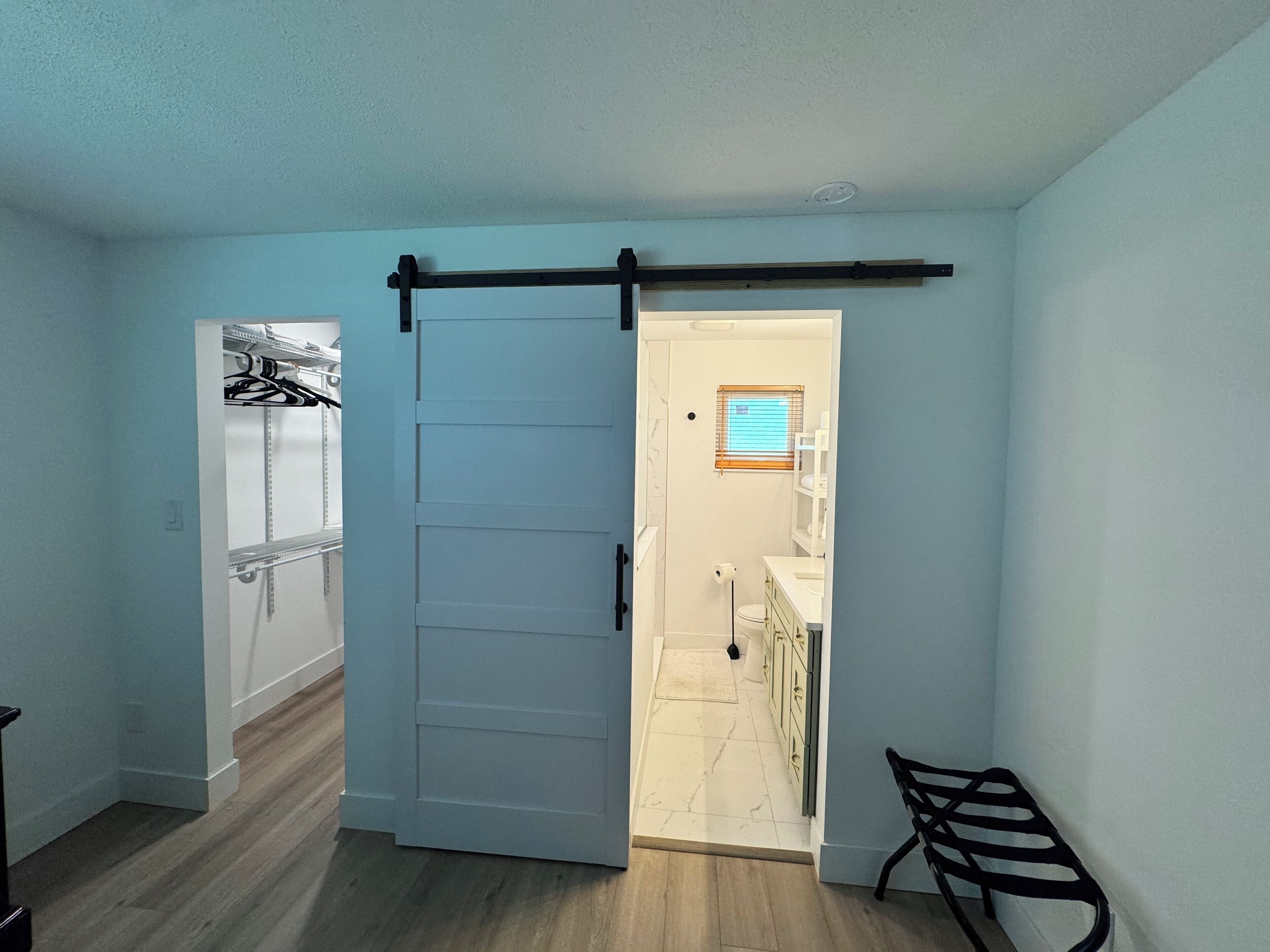 A room with a sliding door leading to a bathroom, a bench, and a shelf with items.