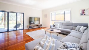 Ein geräumiges Wohnzimmer mit grauem Sofa, einem Couchtisch und einem Flachbildfernseher auf einem Holzschrank.