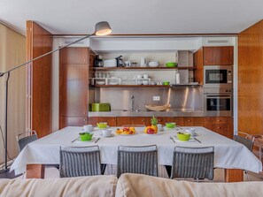 Une cuisine moderne dotée d’appareils électroménagers intégrés, une table à manger pour quatre personnes et une grande fenêtre.