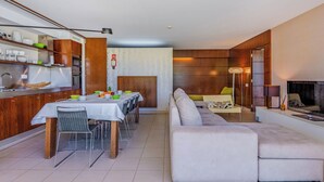 Ein modernes Wohnzimmer mit Sofa, Essbereich mit Tisch und Stühlen sowie Küchenzeile mit Schränken und Geräten.