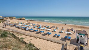 Ein Strand mit Liegestühlen, Sonnenschirmen, einem hölzernen Steg und einem Massagezelt.