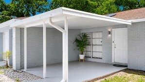 Una casa moderna con un porche cubierto, paredes de ladrillo blanco y un ventanal grande.