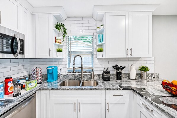 A modern kitchen with white cabinets, a stainless steel sink, and a marble countertop.