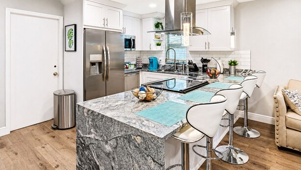 Una cocina moderna con una isla central, electrodomésticos de acero inoxidable y taburetes de bar.