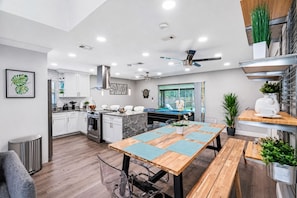 A modern kitchen with white cabinets, a built-in oven, and a dining area with a wooden table and chairs.