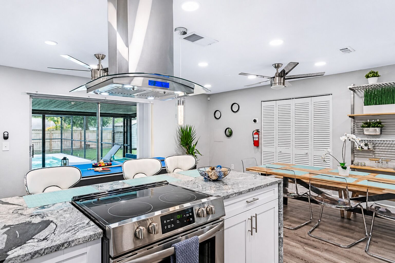 A modern kitchen with a built-in stove, a dining area with a wooden table, and a view of a backyard swimming pool.