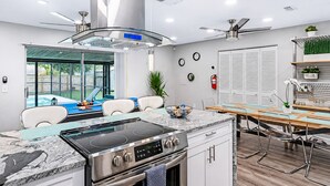 Una cocina moderna con estufa integrada, un comedor con mesa de madera y vista a una piscina en el patio trasero.