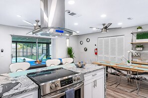 A modern kitchen with a built-in stove, a dining area with a wooden table, and a view of a backyard swimming pool. - Screened Heated Pool, Sleeps 12 | Game Room, 10 Min to Hard Rock Casino (Seffner)