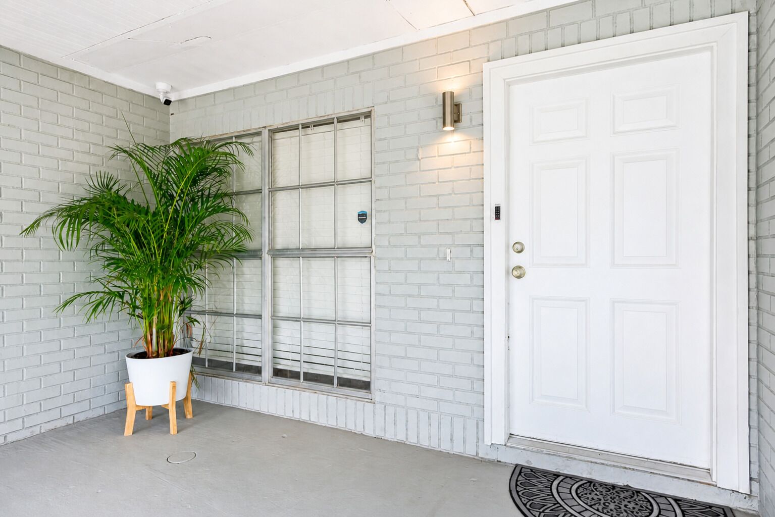 A white door with a keypad lock, a potted plant, and a window with blinds.