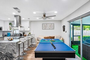 A modern kitchen with a pool table, bar stools, and a dining area with a sofa.