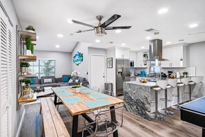 A modern kitchen with a dining area, a ceiling fan, and bar stools.
