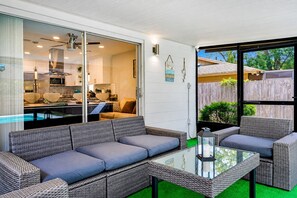 A modern outdoor living area with wicker furniture, a glass table, and a view of the backyard.