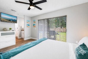A bedroom with a bed, a ceiling fan, a TV, and a view of the backyard through a sliding door.