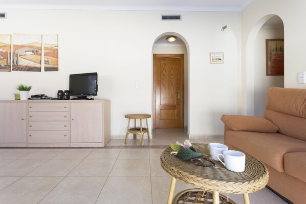 A living room with a sofa, a wicker coffee table with cups, a television on a cabinet, and a door leading to another room. - Ref. VINYA: Ground floor house with swimming pool. (L'Escala)