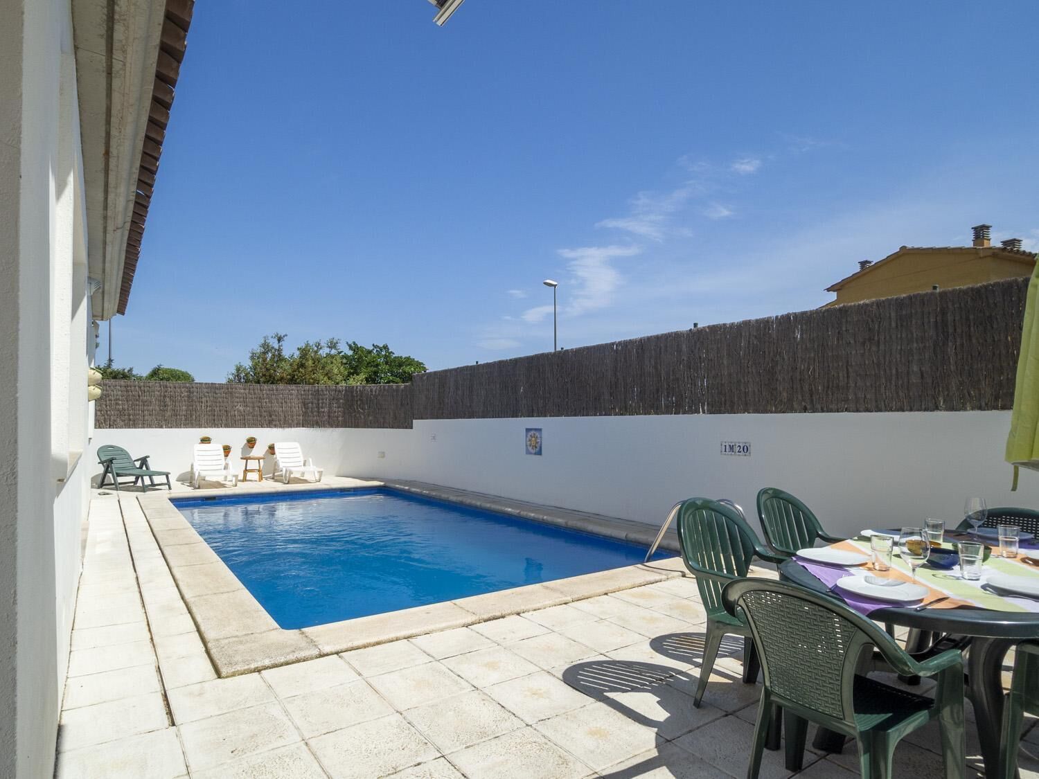 Une piscine avec une terrasse carrelée, une table entourée de chaises et un espace abrité avec des parasols.