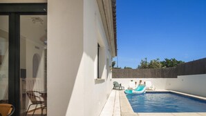 Ein Swimmingpool mit Liegestühlen und einem kleinen Luftmatratze, umgeben von einer weißen Mauer und einer gefliesten Terrasse.