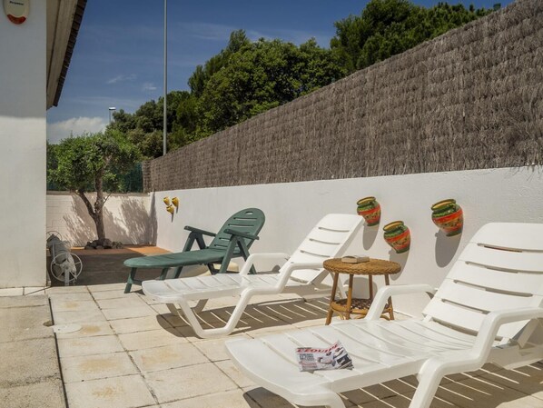 A sunlit outdoor seating area with white lounge chairs, a small round table, and decorative vases on a wall. - Ref. VINYA: Single-story house with a swimming pool. (L'Escala)