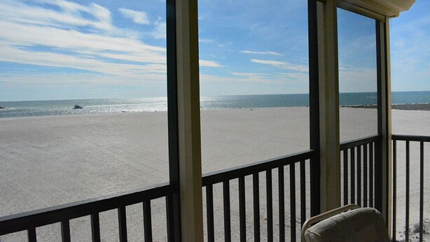 A beach view from a balcony with a chair.