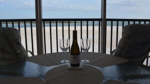 A table with a bottle of wine and two glasses, overlooking a beach.