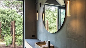 Un baño moderno con un espejo grande, un lavabo rectangular e iluminación colgante.