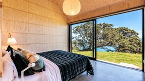 A bedroom with a large window, a bed with pillows, and a hanging light fixture. - Mawhiti - Architecture & Beach Access Near Oneroa (Waiheke Island)