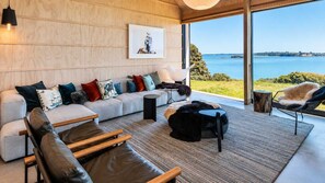A modern living room with a large window overlooking a body of water, a sofa set, and a coffee table. - Mawhiti - Architecture & Beach Access Near Oneroa (Waiheke Island)