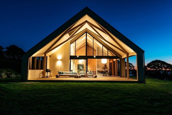 A modern, well-lit house with a large open interior, a dining area, and a visible living room with furniture. - Mawhiti - Architecture & Beach Access Near Oneroa (Waiheke Island)