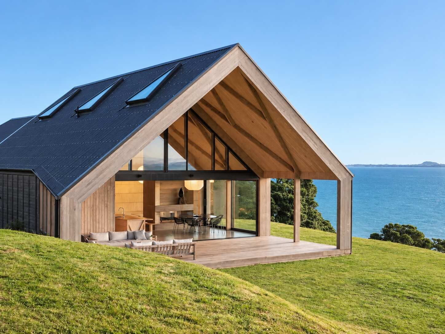 A modern house with a sloped roof, large glass windows, and a view of the sea.
