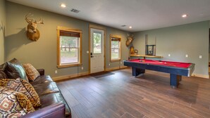 A room with a pool table, leather sofa, and deer antlers on the wall. - Hot Tub, Game Room & More! Lakefront Home in Afton (Afton)