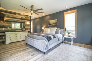 Een slaapkamer met een bed, nachtkastjes, een dressoir, een plafondventilator, een raam en een schilderij aan de muur.