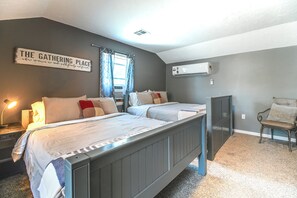 Een slaapkamer met twee bedden, een nachtkastje met lamp, een stoel, een raam met gordijnen en een airconditioning.
