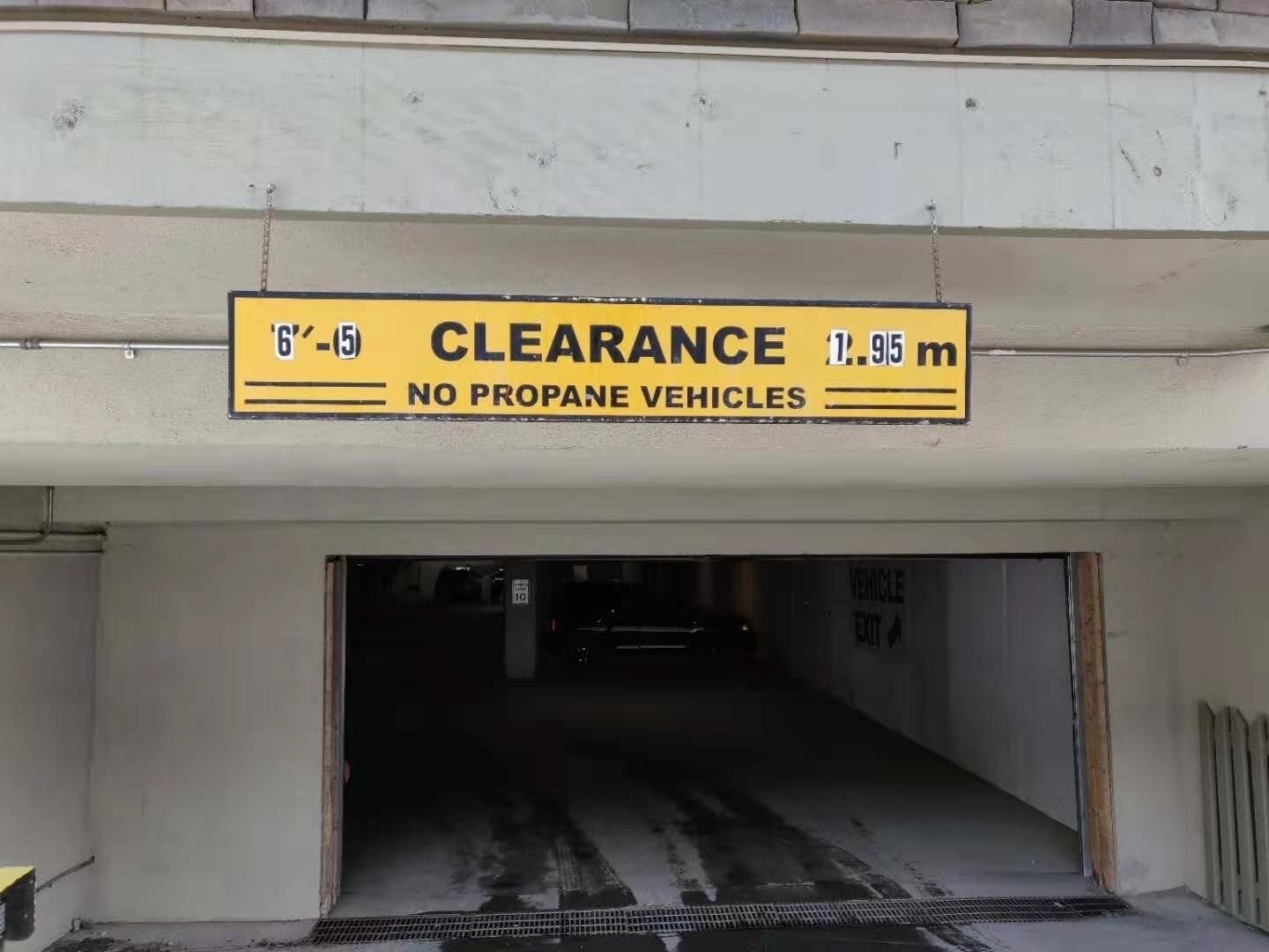 A parking garage entrance with a clearance sign indicating 6'-5" and 1.95 meters height limit, and a no propane vehicles warning.