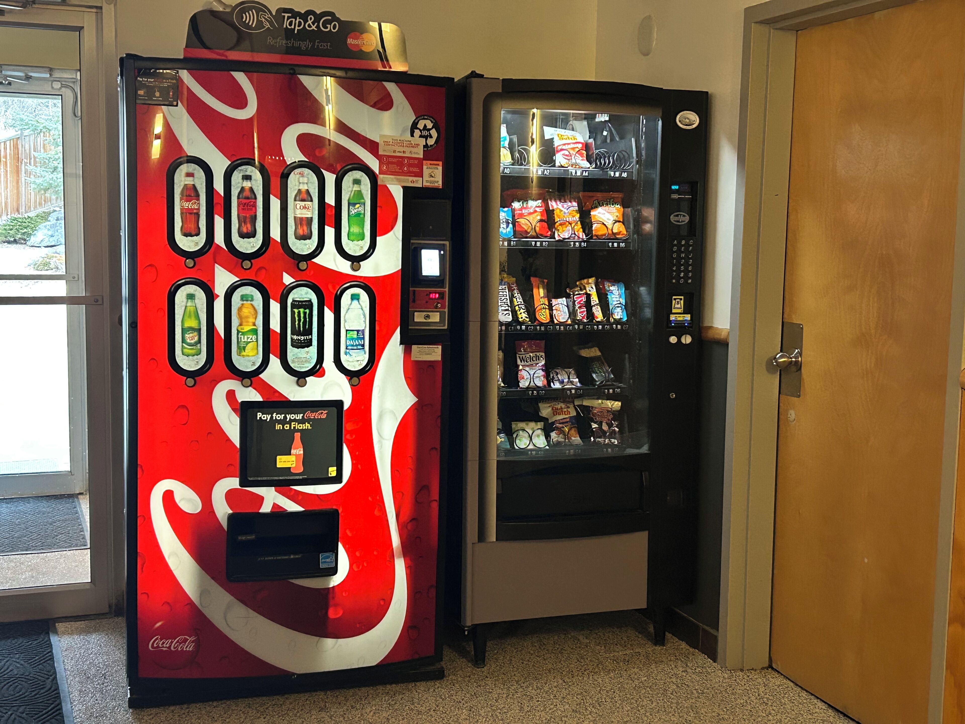 Un distributeur automatique de boissons de la marque Coca-Cola, équipé d’un terminal de paiement, et un autre distributeur automatique de snacks situé à côté.