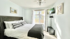 Une chambre à coucher avec un lit, un ventilateur de plafond, une télévision et une fenêtre avec des rideaux.