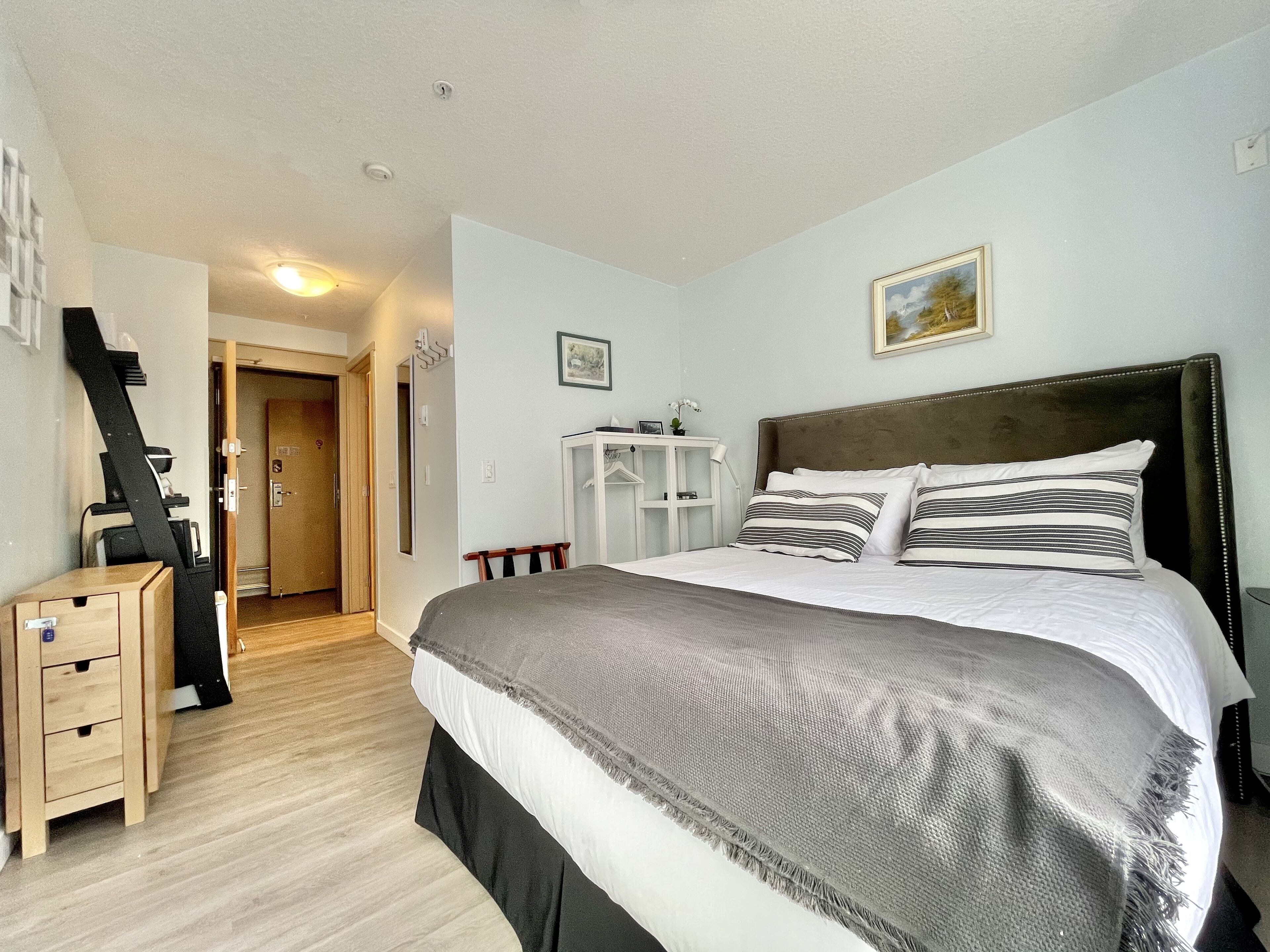 A bedroom with a large bed, a wooden nightstand, a desk, and a wardrobe.