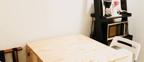 A small wooden table with two white chairs, a black shelf with a coffee maker, and a microwave.