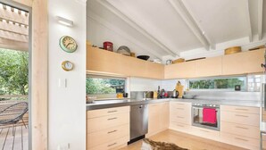 A modern kitchen with light wood cabinets, stainless steel appliances, and a large window. - Palm Views - 3-Minute walk to Palm Beach (Waiheke Island)