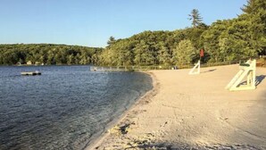 Une plage avec une tour de surveillance, une eau claire et une colline boisée en arrière-plan.