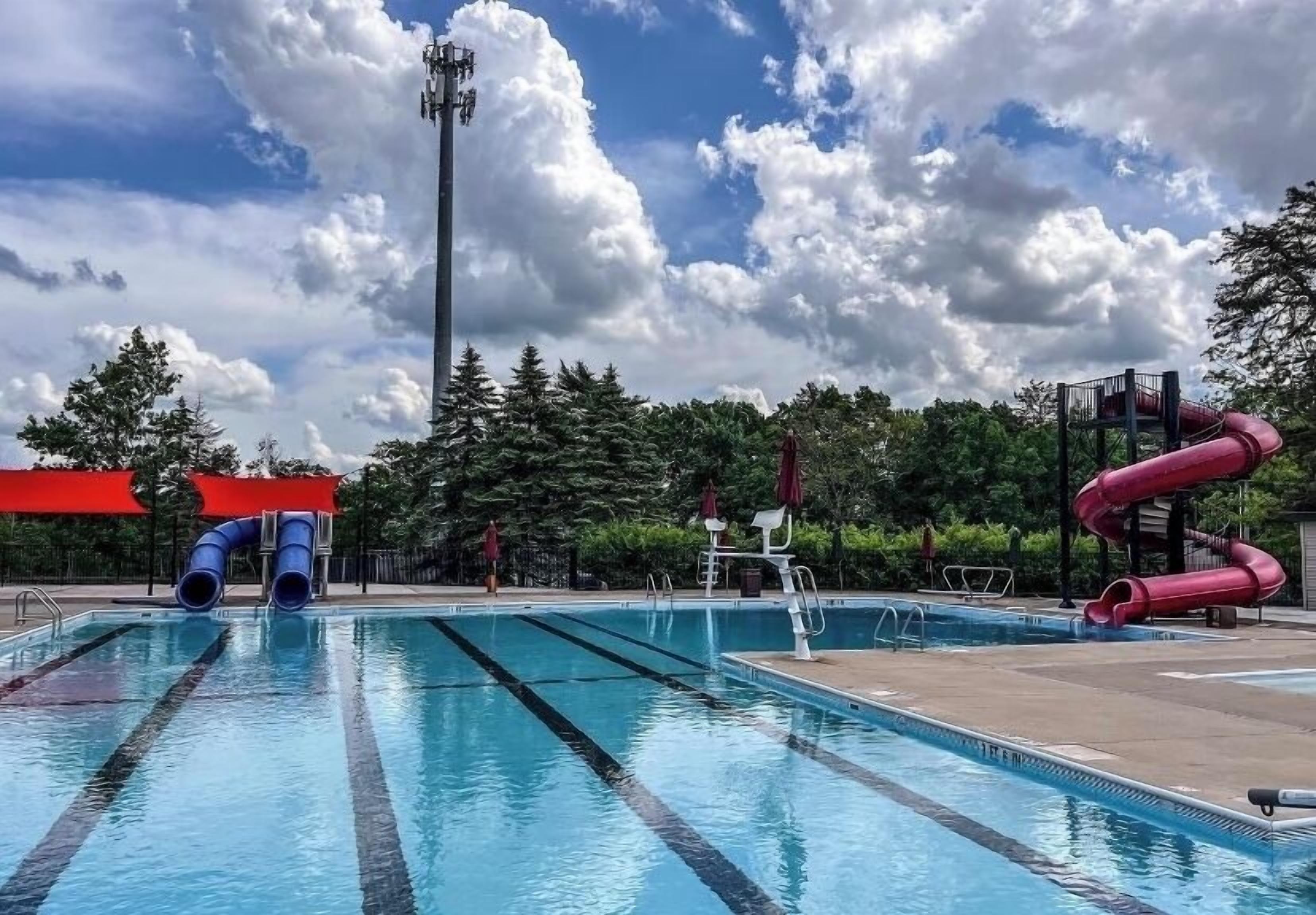 A swimming pool with two slides, surrounded by trees and a clear sky.