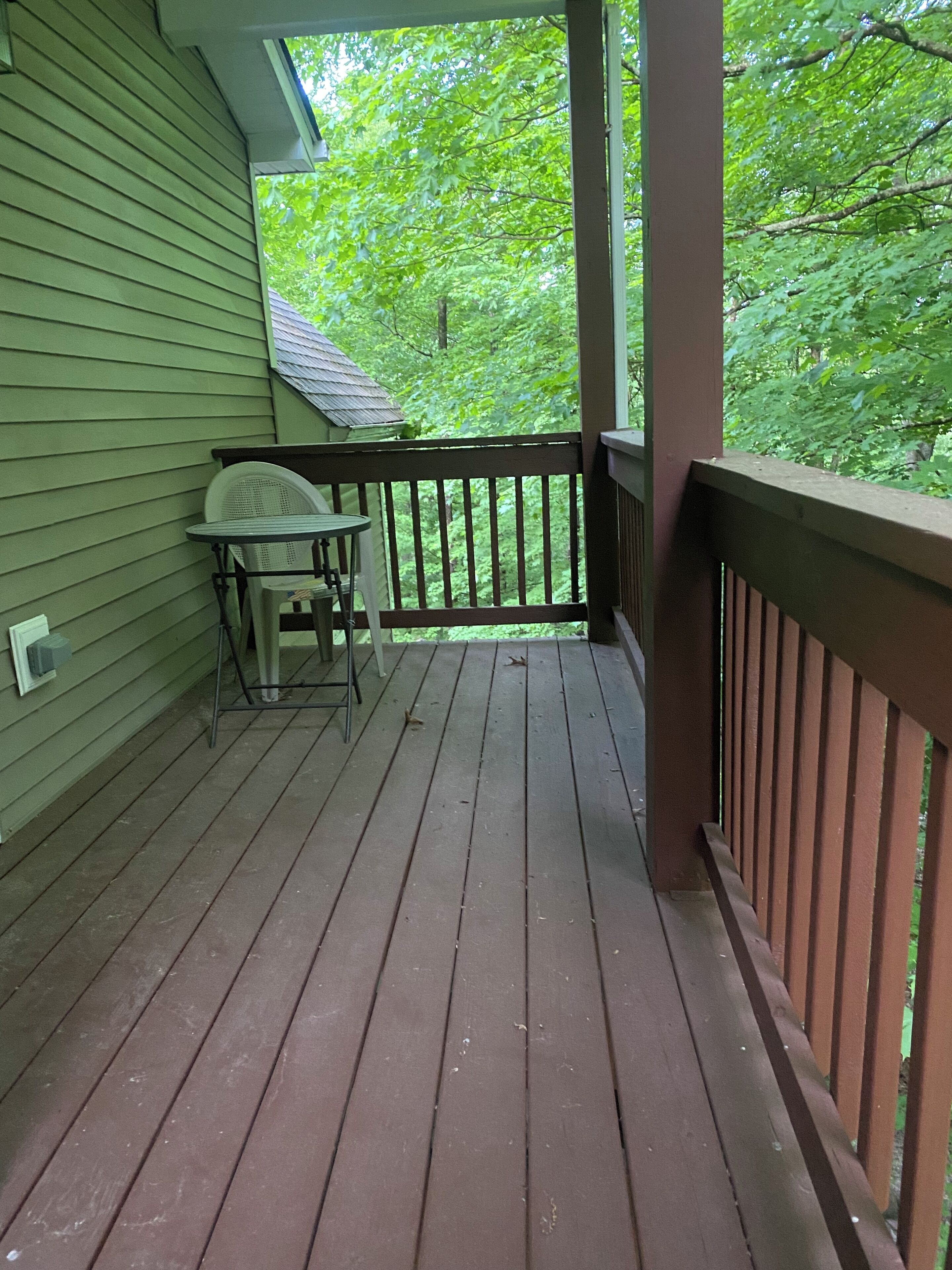 Une terrasse en bois, agrémentée d’une table et de chaises, entourée d’une balustrade et offrant une vue sur un paysage verdoyant et luxuriant.