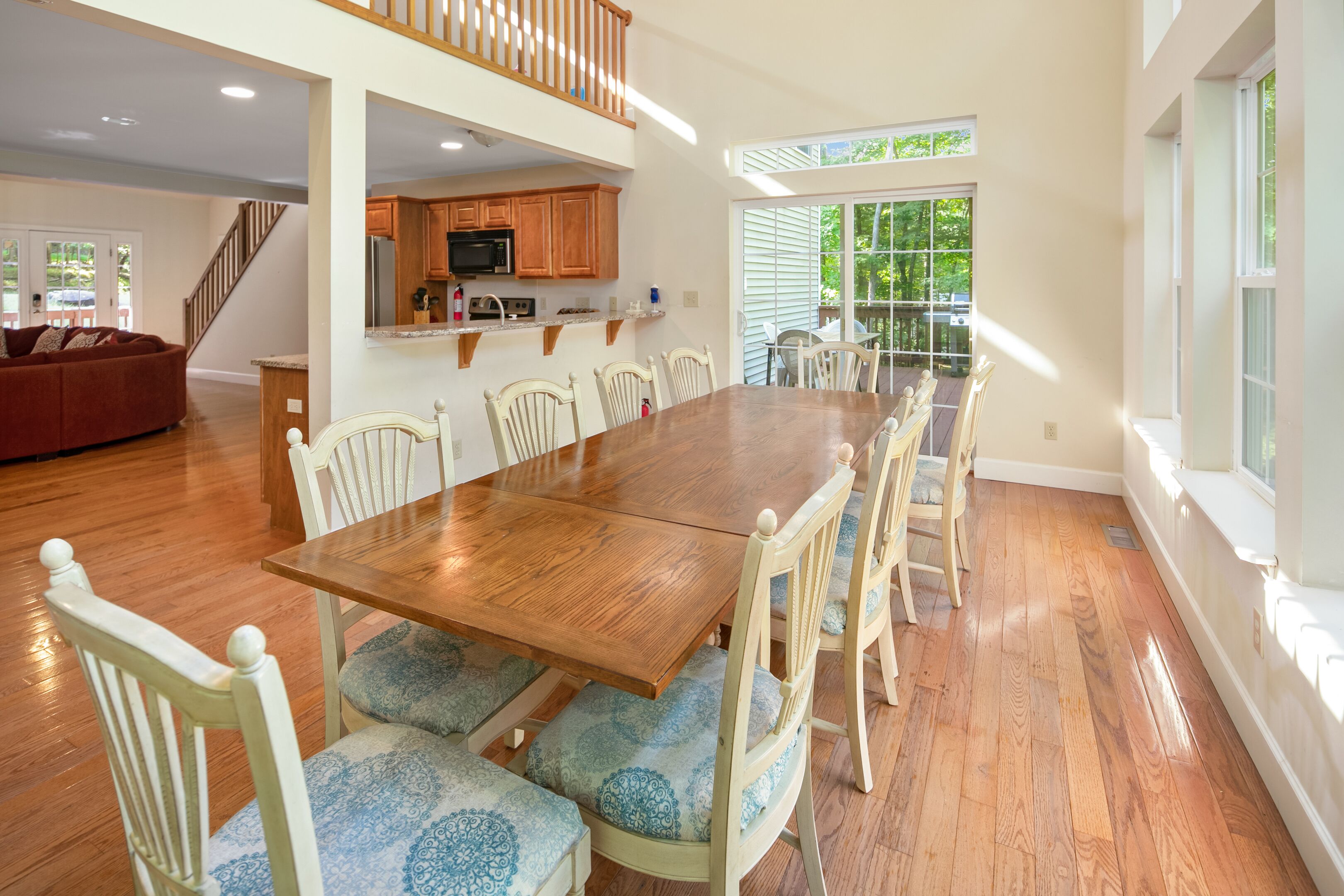 Un comedor amplio con una mesa de madera y sillas blancas, una cocina con armarios de madera y una escalera que conduce a un nivel superior.