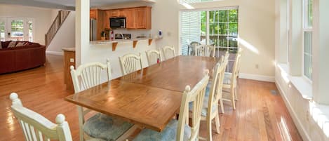 Un comedor amplio con una mesa de madera y sillas blancas, una cocina con armarios de madera y una escalera que conduce a un nivel superior.