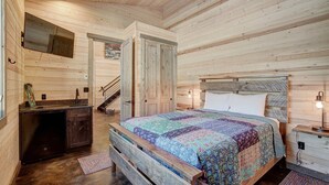 Un dormitorio de cabaña de madera con una cama, mesitas de noche, un aparador, un espejo y una escalera.