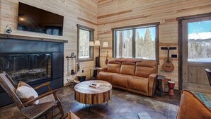 Un interior de cabaña acogedor, con chimenea, sofá de cuero y una mesa de comedor.