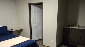 Quarto com cama, porta e um espaço com cozinha.