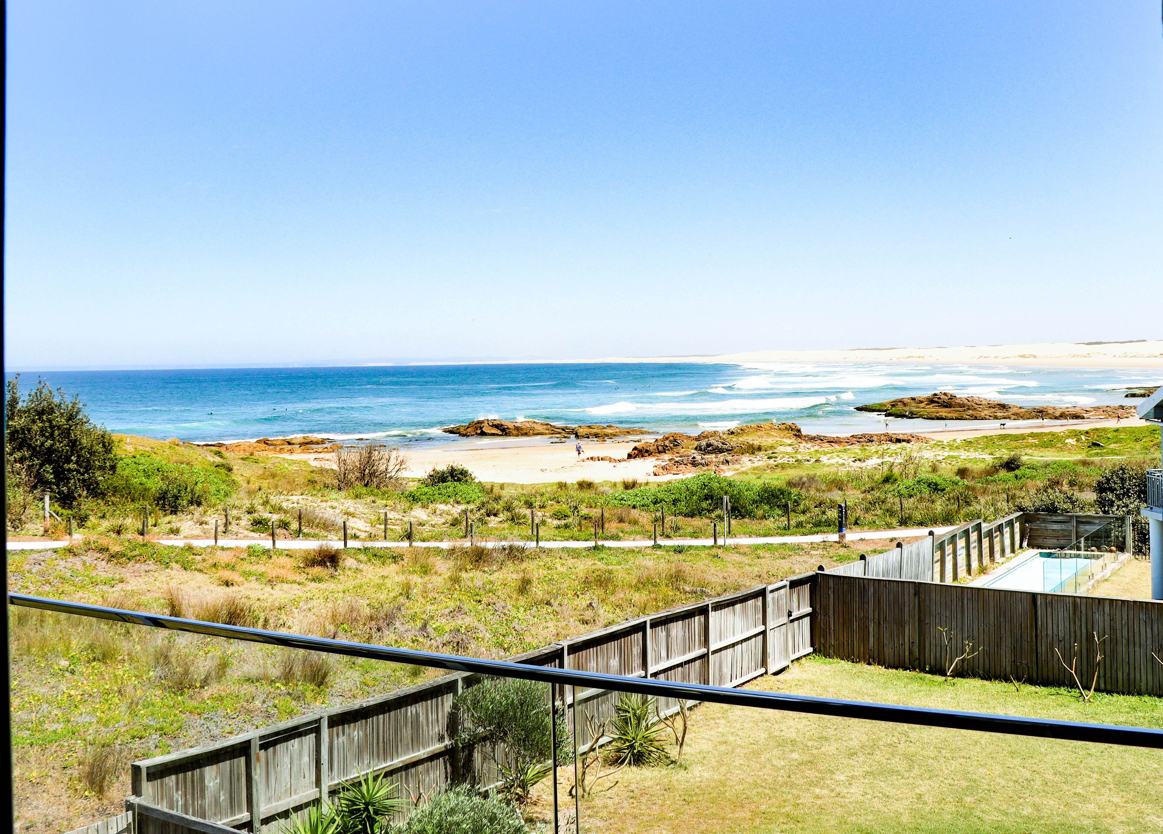 A coastal view with a sandy beach, rocky outcrops, and a clear blue sky.